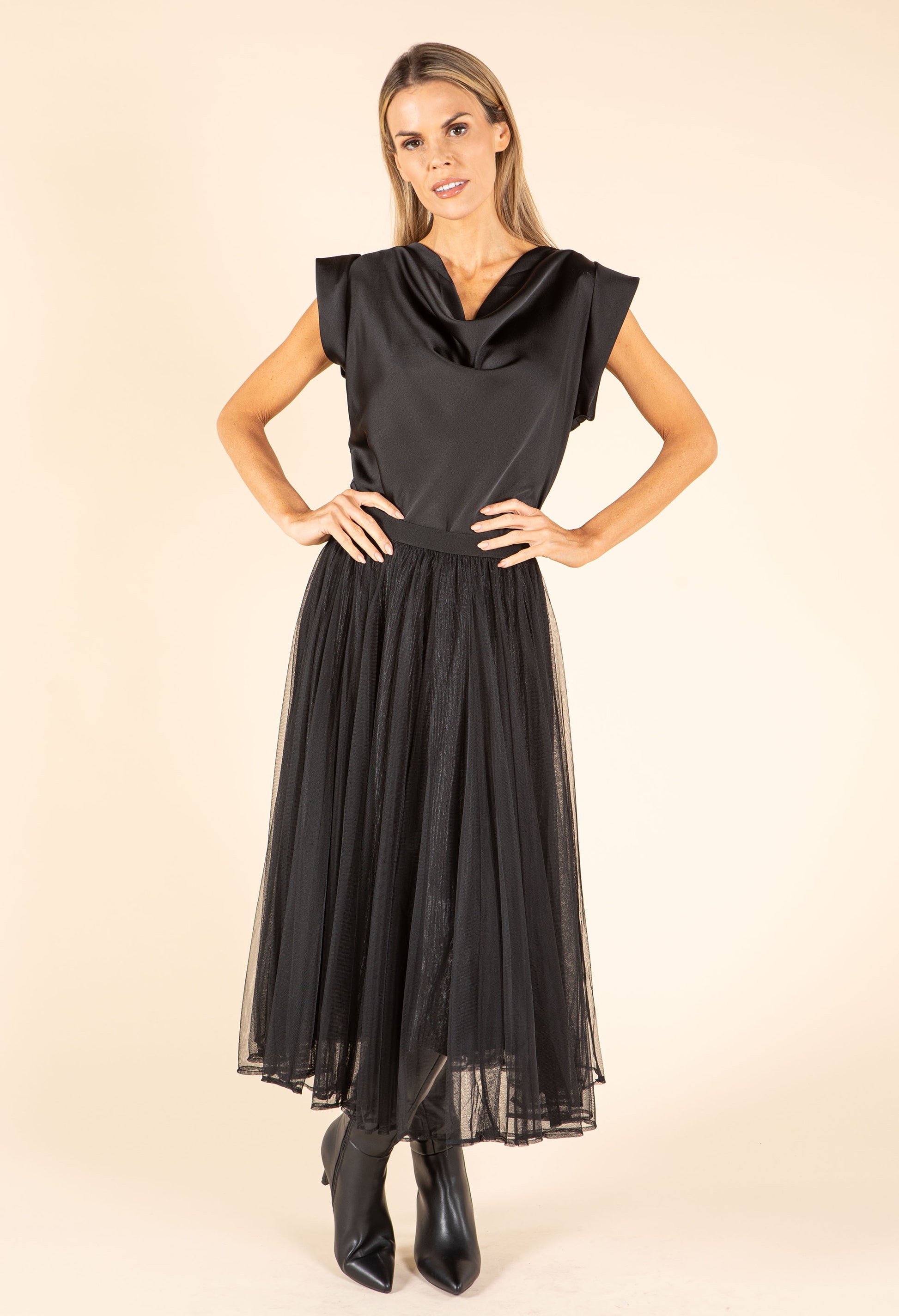 Woman wearing a black dress with a cowl neckline on a beige background