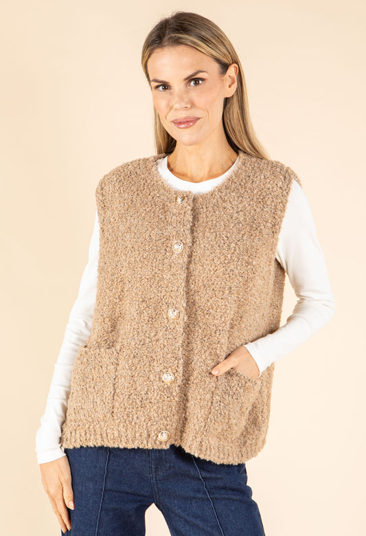 Woman wearing a beige knitted vest over a white shirt on a beige background