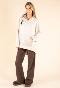 Woman wearing a beige hooded jacket and brown pants on a beige background