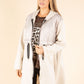 Woman wearing a long white coat over a patterned top on a beige background