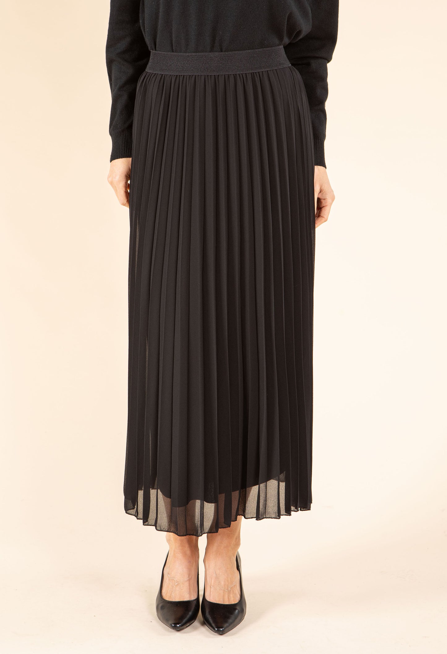 Person wearing a black pleated skirt on a beige background