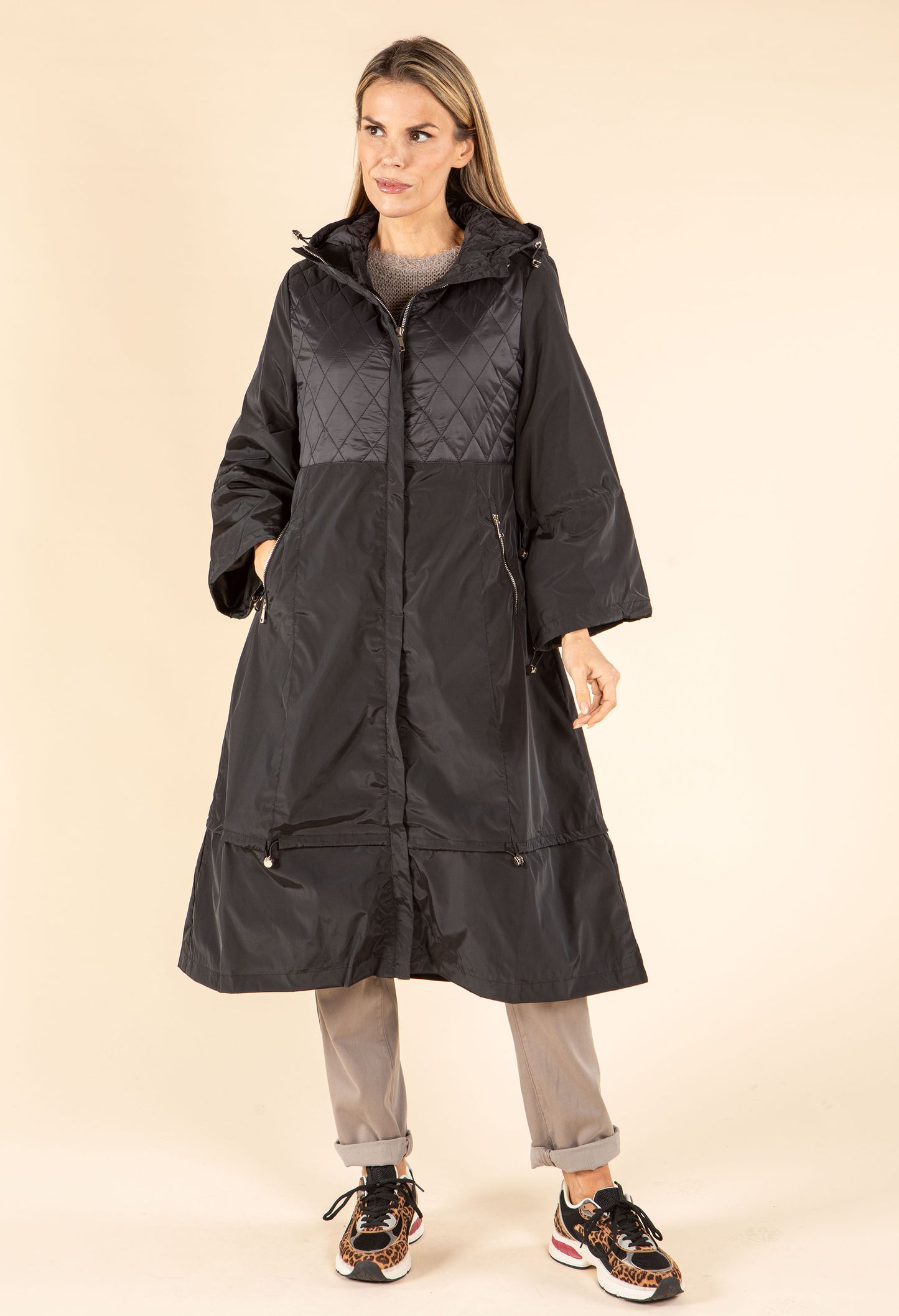 Woman wearing a long black coat on a beige background