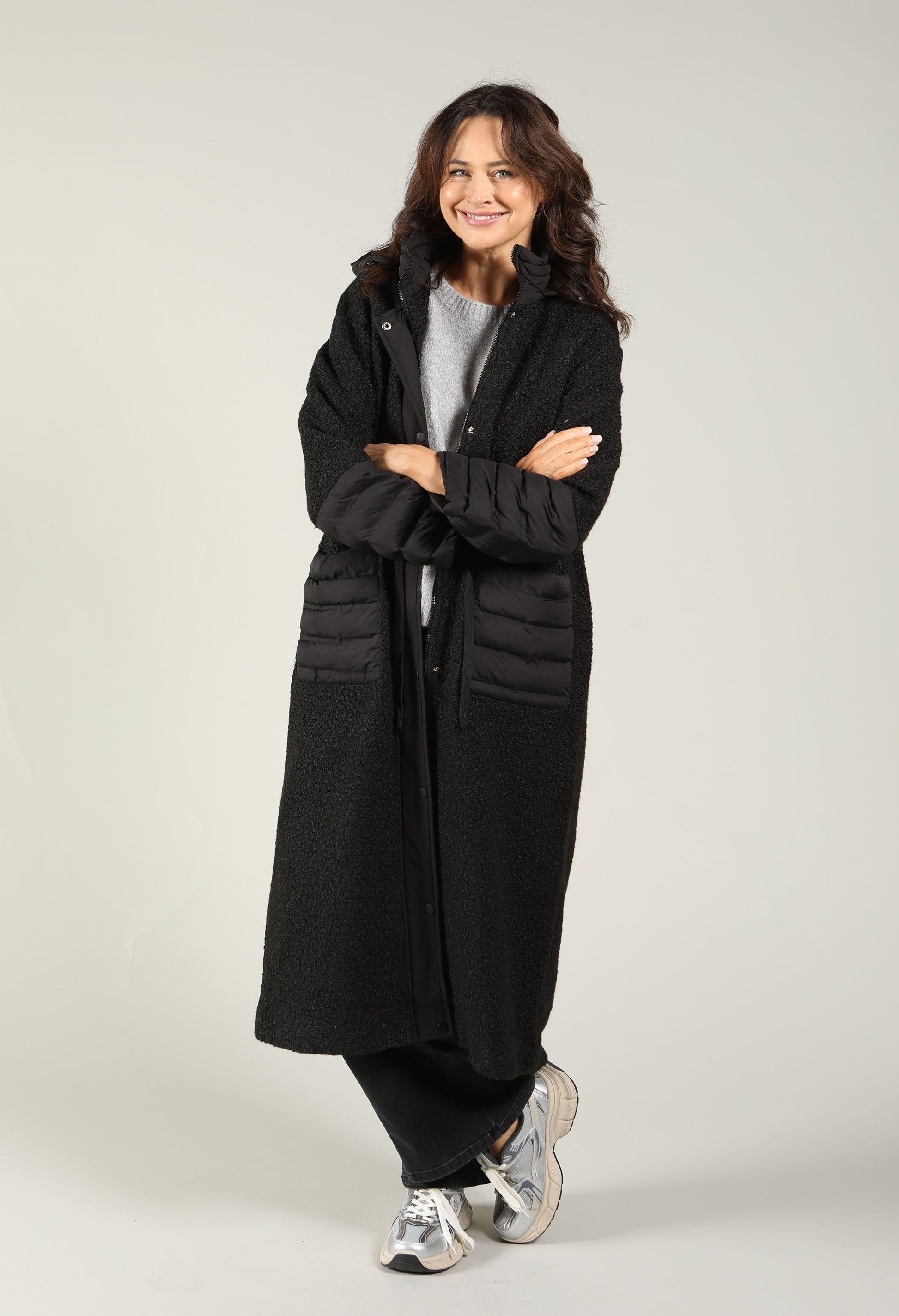 Woman wearing a long black coat on a plain background