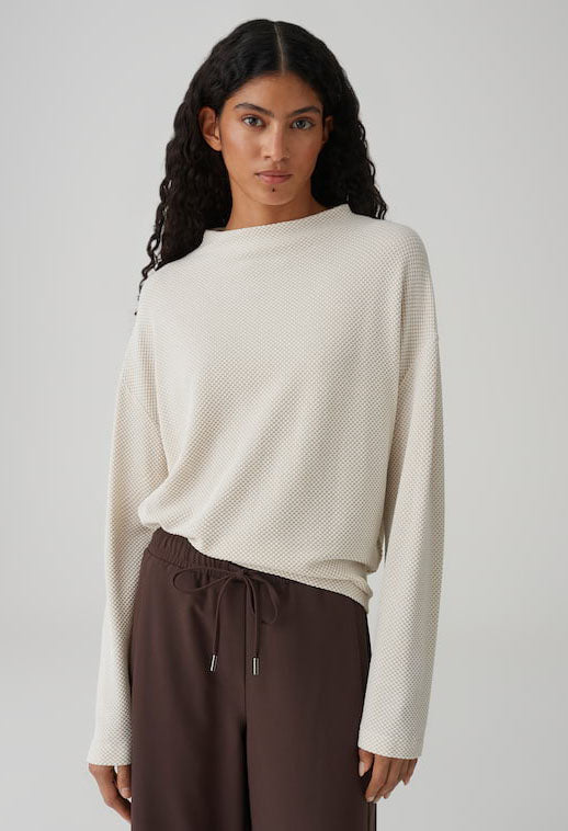 Woman wearing a white textured sweater and brown pants on a plain background