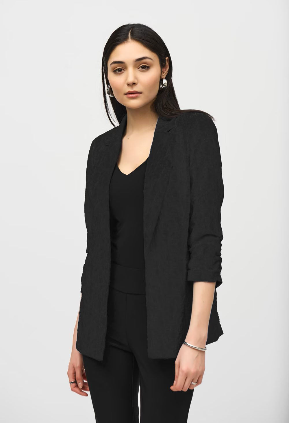 Woman wearing a black blazer over a black top and pants on a white background