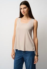 Woman wearing a beige sleeveless top and blue jeans against a plain background