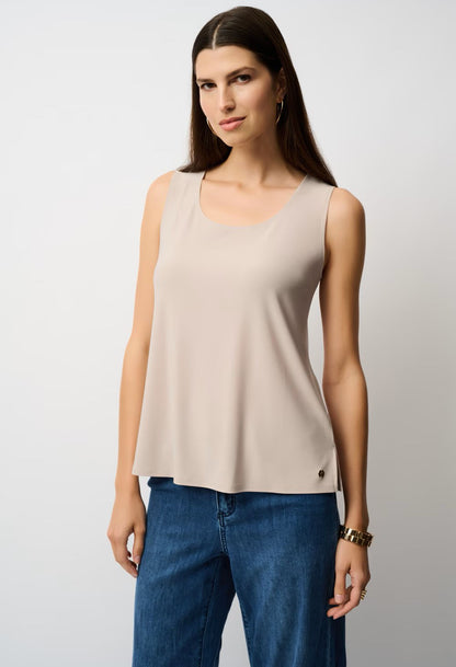 Woman wearing a beige sleeveless top and blue jeans against a plain background