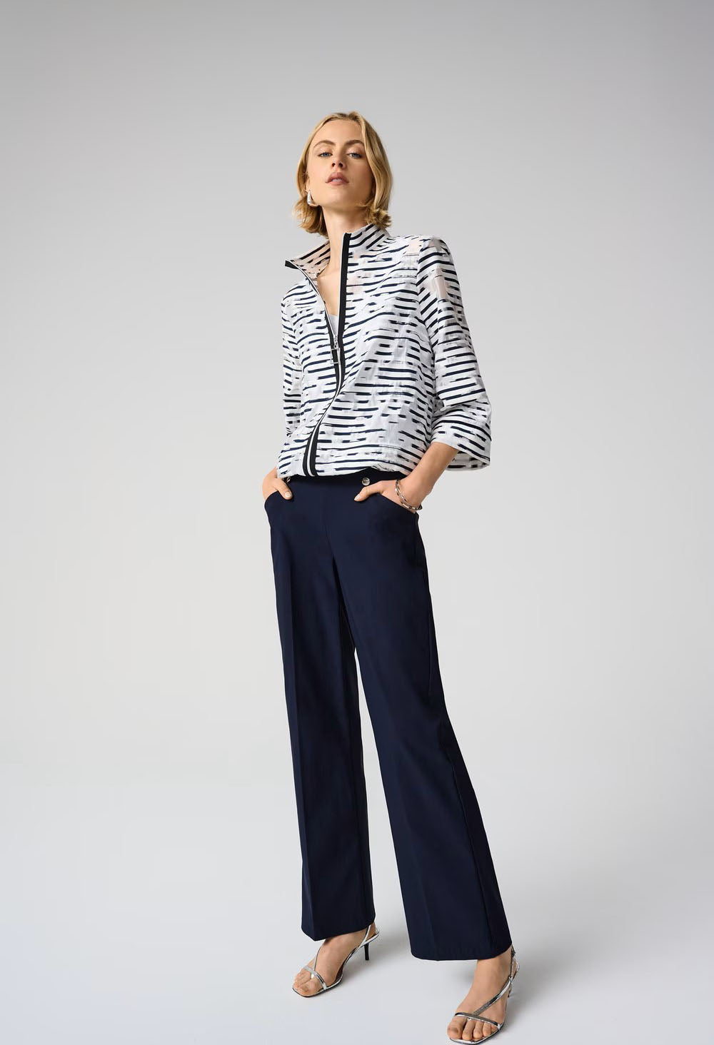 Woman wearing a black and white striped jacket and navy pants on a gray background