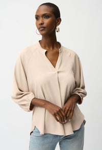 Woman wearing a beige blouse and light blue jeans against a white background