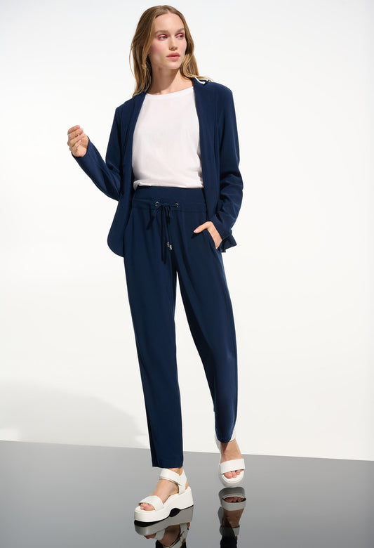 Woman wearing a navy blue outfit with a white top on a plain background