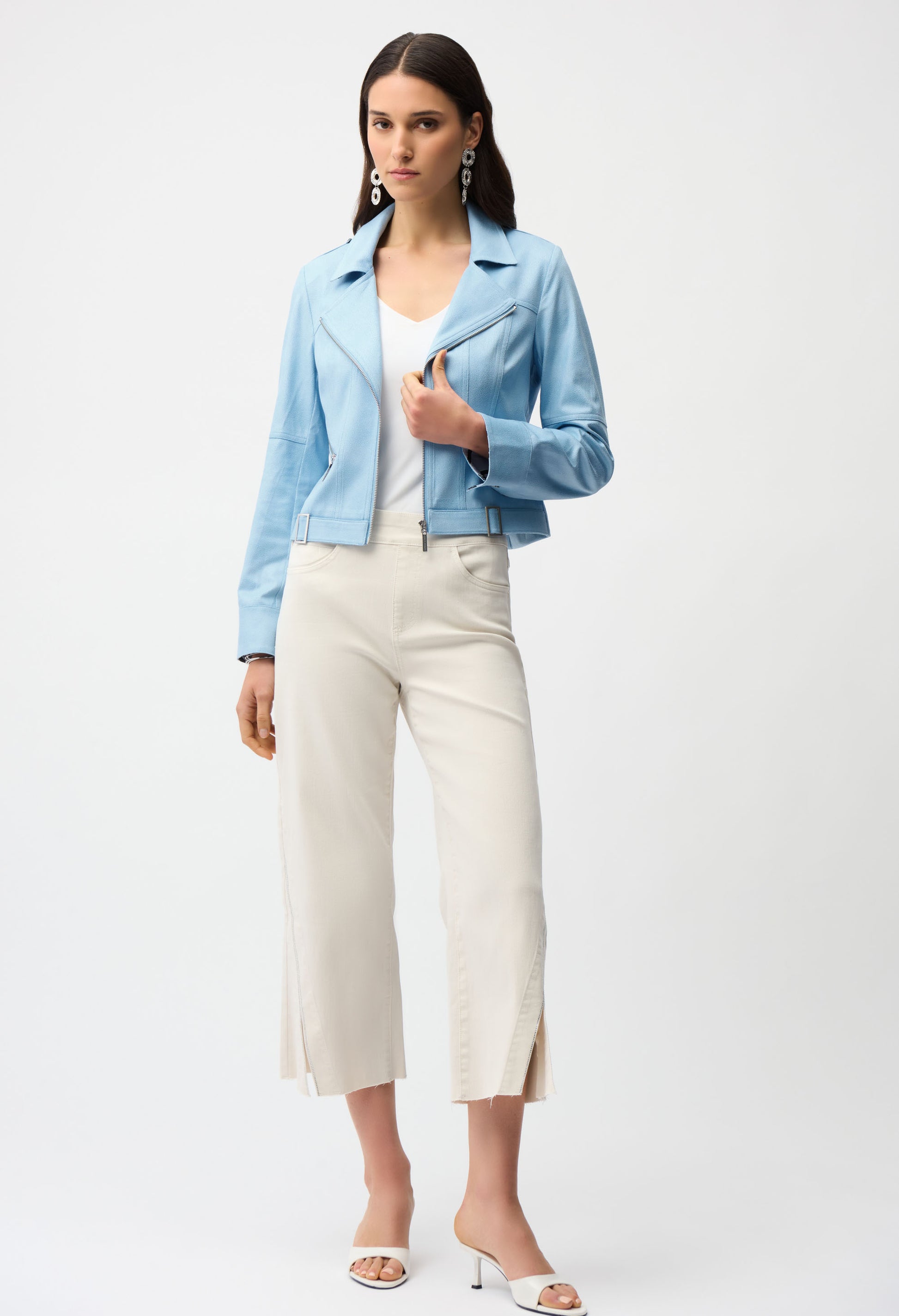 Woman wearing a light blue jacket, white top, and white pants on a white background