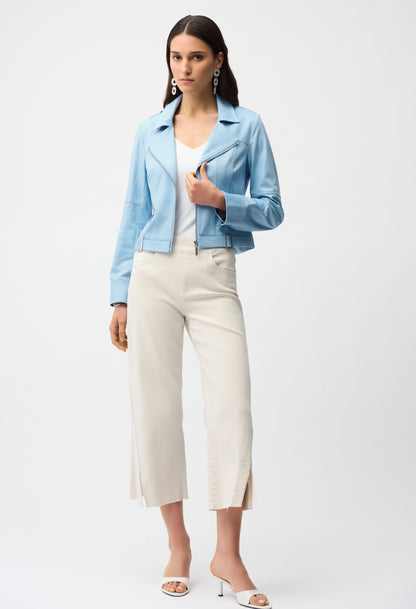 Woman wearing a light blue jacket, white top, and white pants on a white background