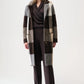 Woman wearing a long, plaid coat over a dark outfit on a white background