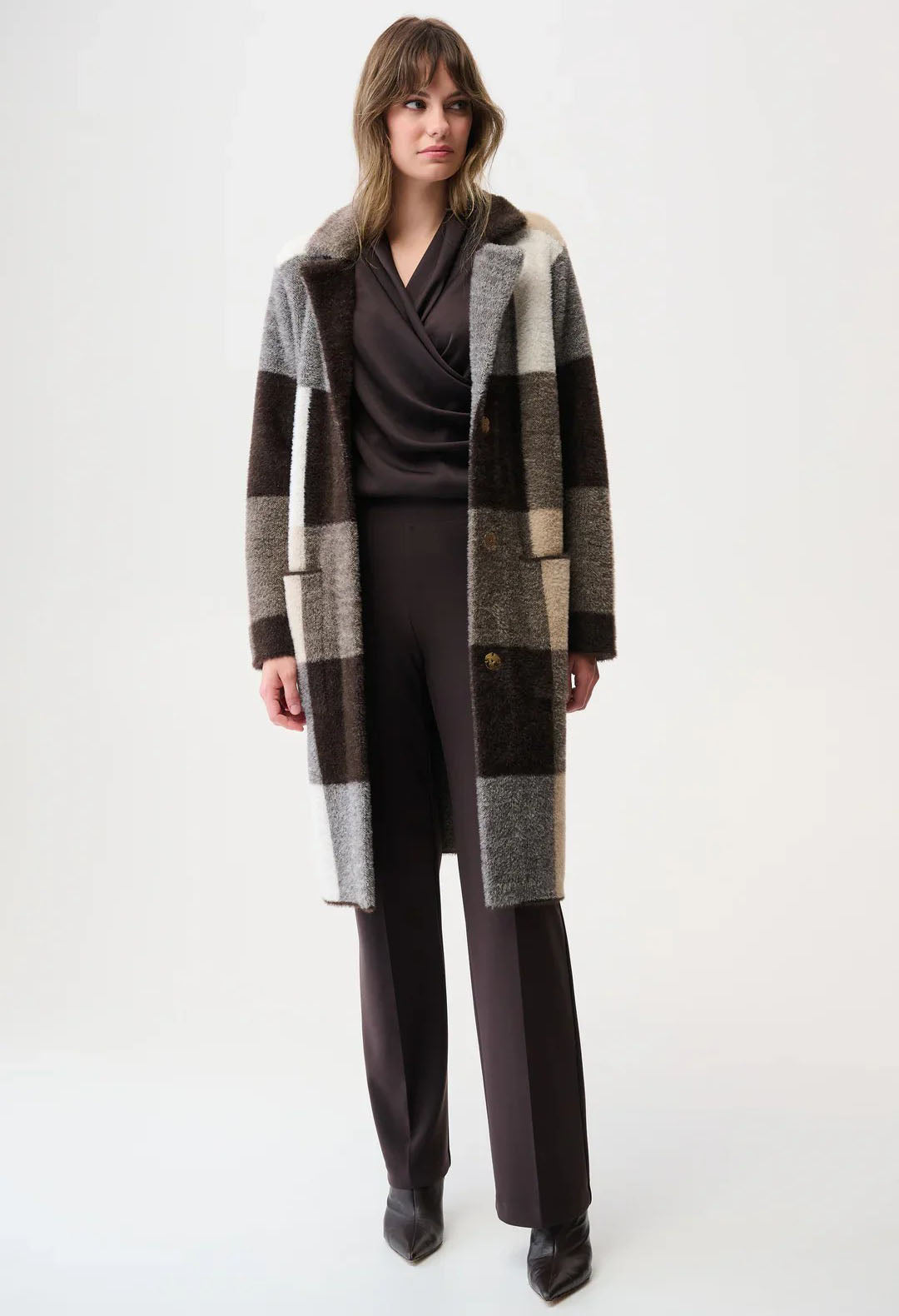 Woman wearing a long, plaid coat over a dark outfit on a white background