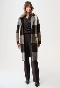 Woman wearing a long, plaid coat over a dark outfit on a white background