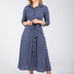 Woman wearing a navy blue dress with white polka dots on a white background
