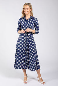 Woman wearing a navy blue dress with white polka dots on a white background