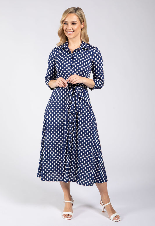 Woman wearing a navy blue dress with white polka dots on a white background
