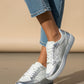 White sneakers with silver accents worn with blue jeans on a neutral background