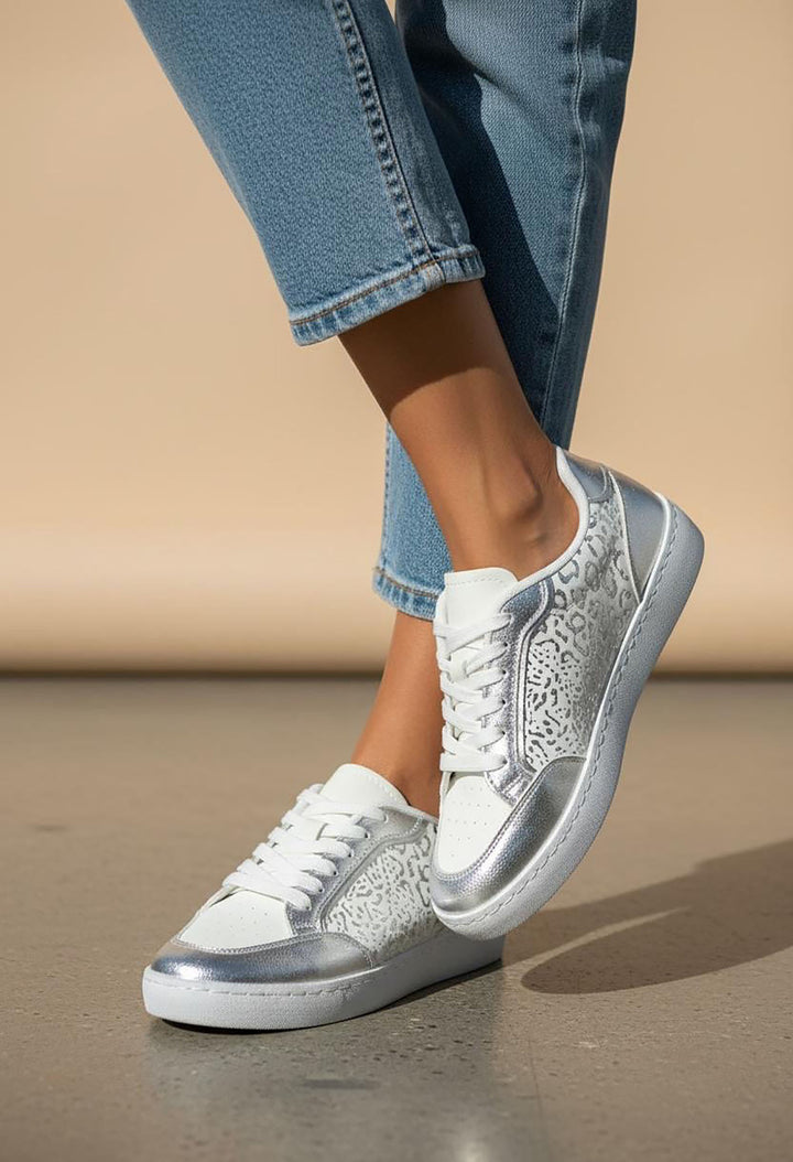 White sneakers with silver accents worn with blue jeans on a neutral background