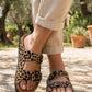 Leopard print sandals worn with beige pants on a wooden floor.