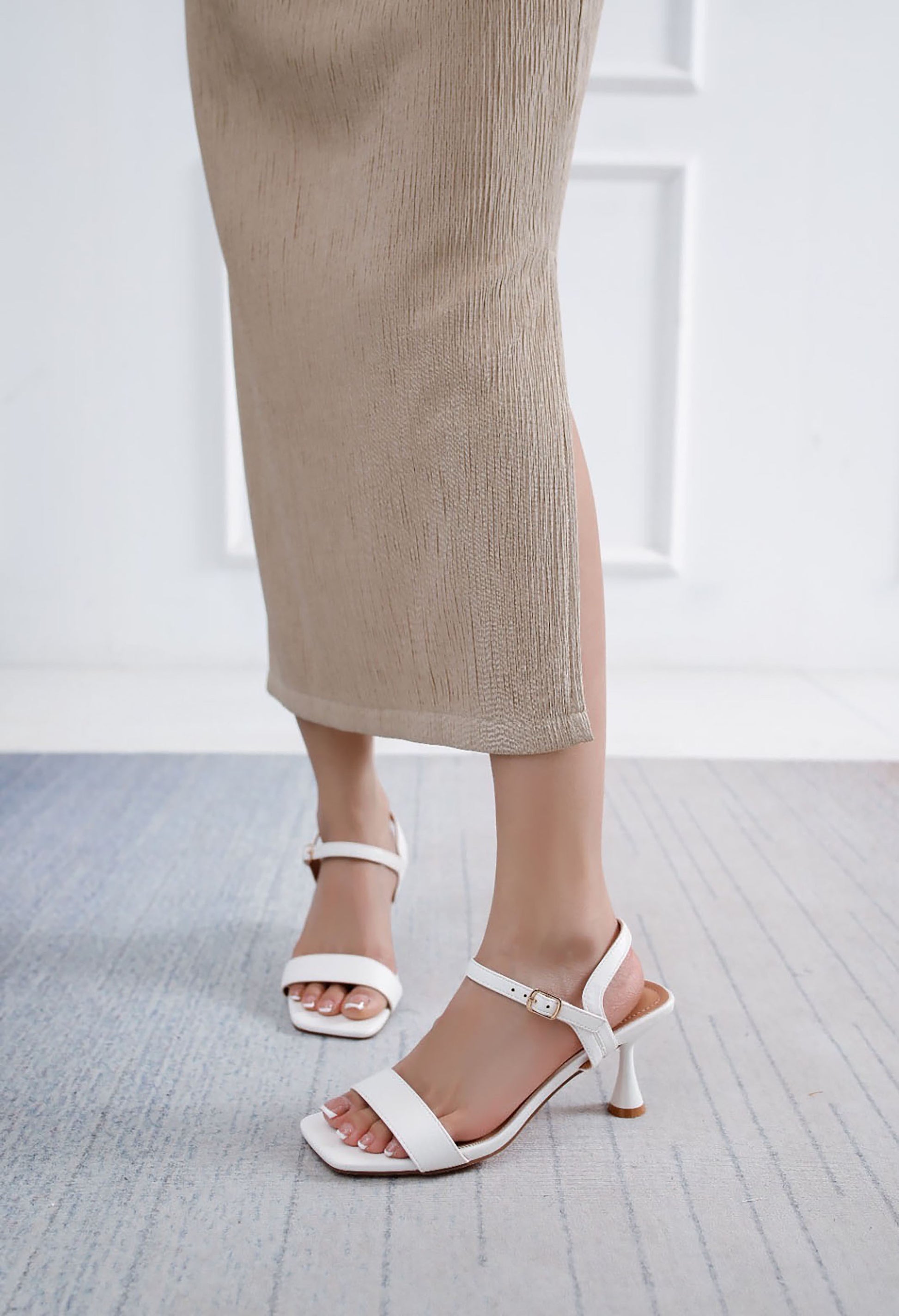 White sandals worn with beige pants on a light gray floor.