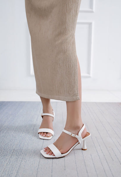 White sandals worn with beige pants on a light gray floor.