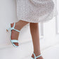 Light blue high-heeled sandals worn with a white dress on a light background