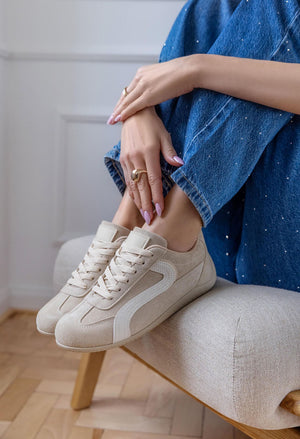 Person wearing white sneakers and blue jeans sitting on a stool indoors.