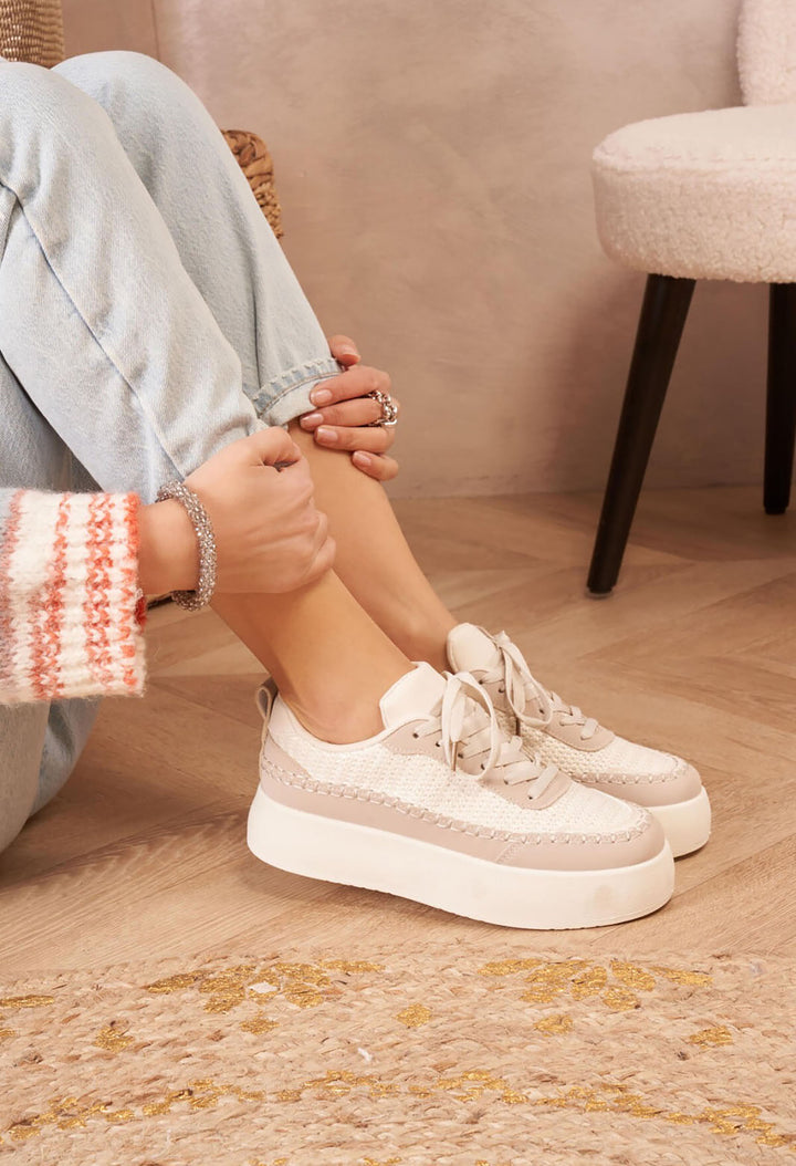 Person wearing white sneakers sitting on a wooden floor with a neutral background