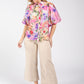 Woman wearing a colorful floral blouse and beige pants on a white background