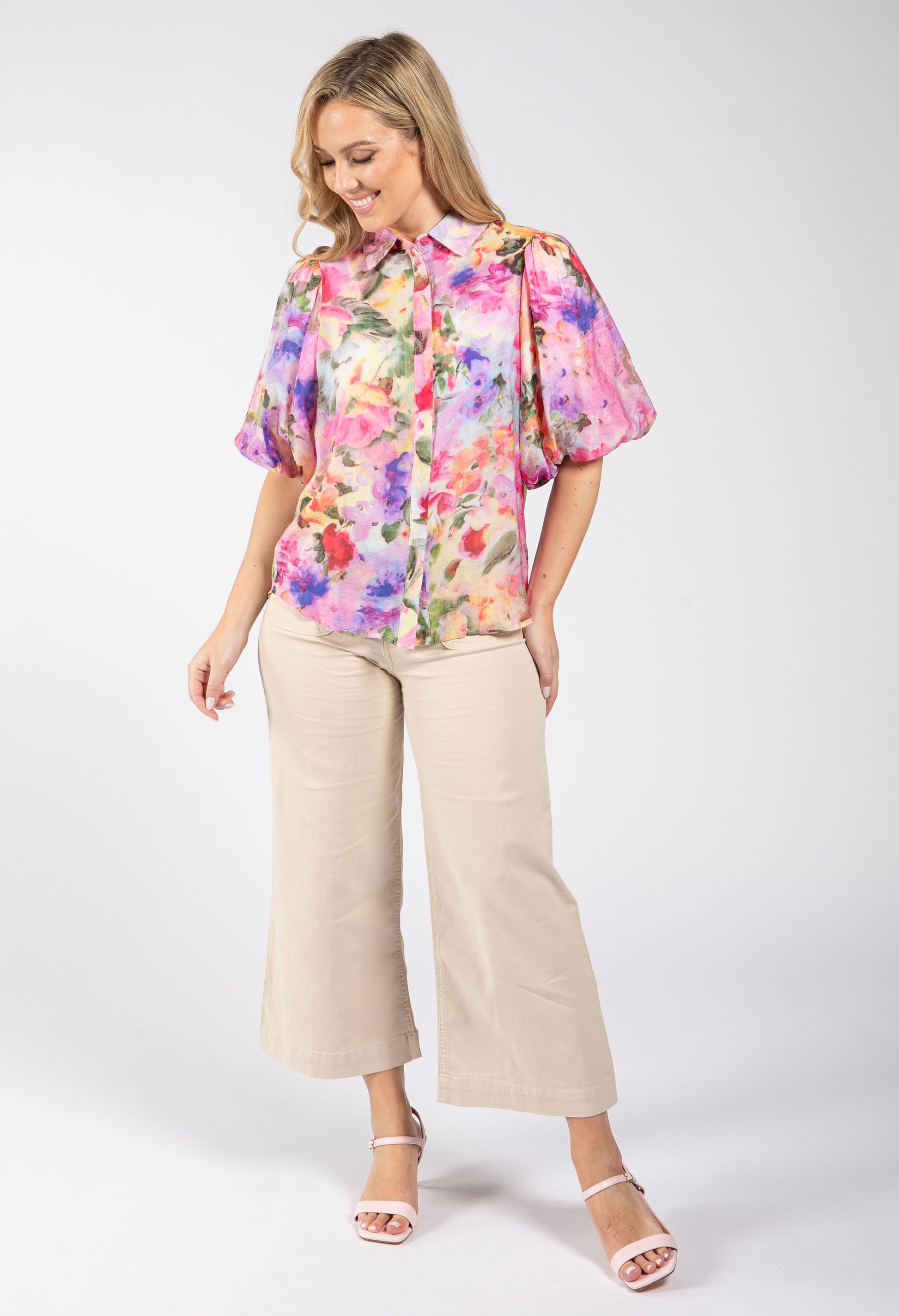 Woman wearing a colorful floral blouse and beige pants on a white background