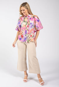 Woman wearing a colorful floral blouse and beige pants on a white background
