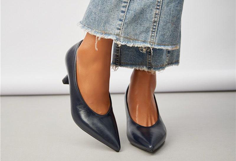 Black high-heeled shoes worn with a denim skirt on a neutral background