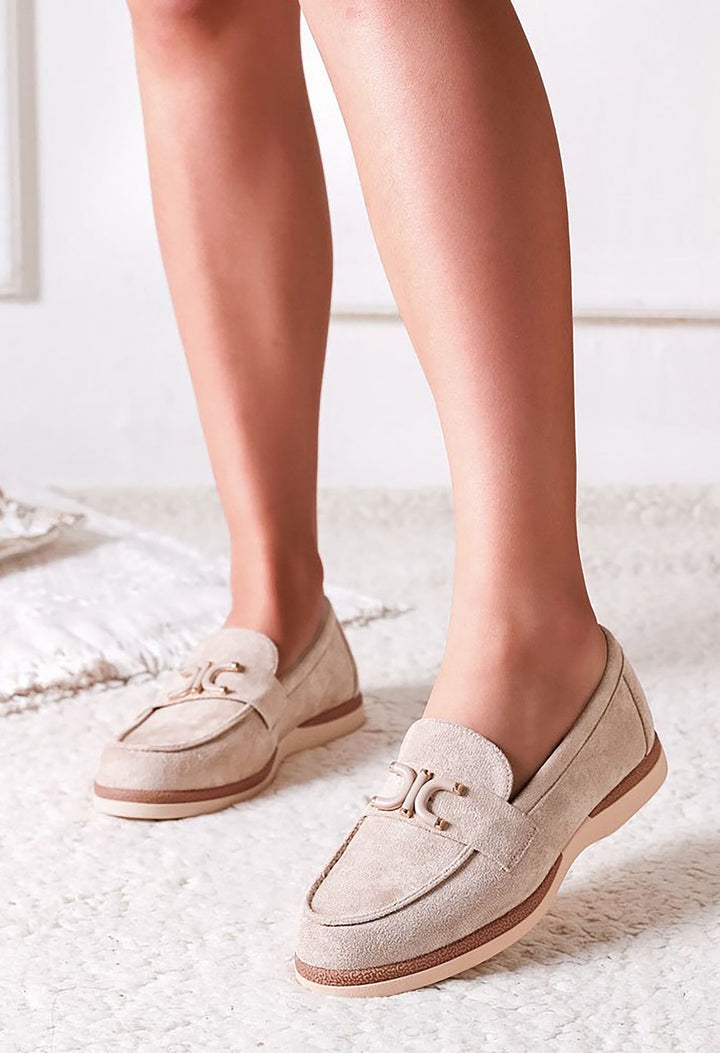 Beige loafers worn by a person on a white carpet