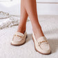 Beige loafers with gold chain details worn by a person on a light background