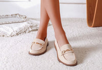 Beige loafers with gold chain details worn by a person on a light background