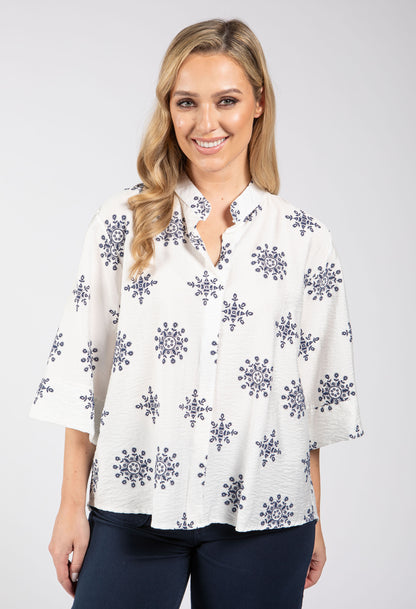 Woman wearing a white blouse with purple floral patterns on a plain background