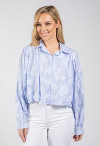 Woman wearing a light blue patterned shirt and white pants on a gray background