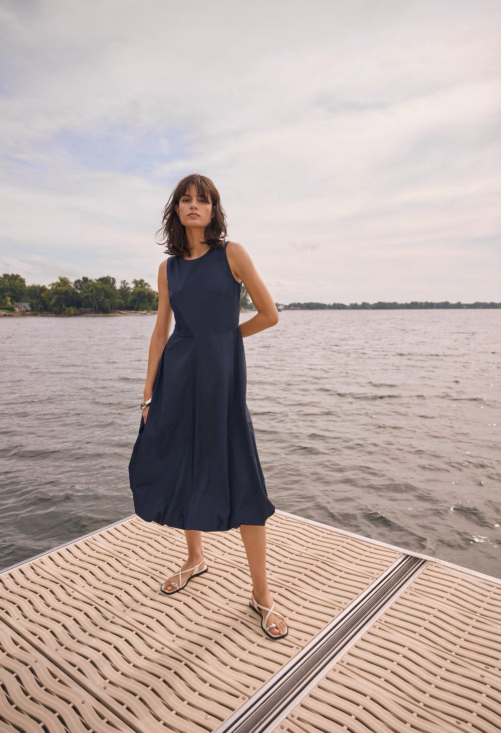 Woman in a navy dress standing on a dock by a body of water.