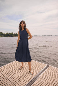 Woman in a navy dress standing on a dock by a body of water.