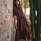Woman in a brown dress standing against a stone wall with cacti in the foreground