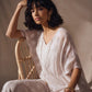 Woman in a white outfit sitting on a wicker chair against a neutral background