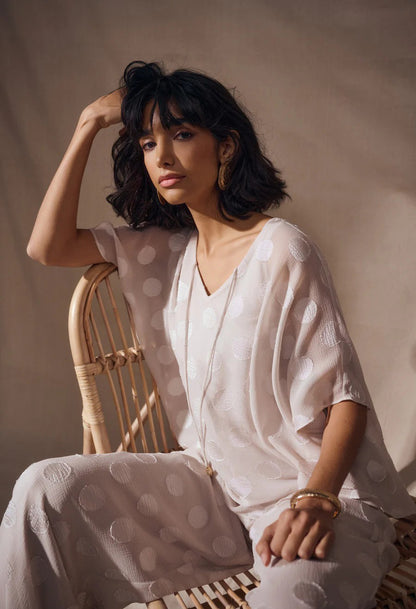 Woman in a white outfit sitting on a wicker chair against a neutral background
