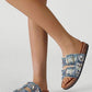 Denim sandals with embellishments worn by a person on a light gray background