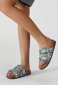 Denim sandals with embellishments worn by a person on a light gray background