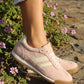Pink sneakers worn on a stone path with flowers in the background