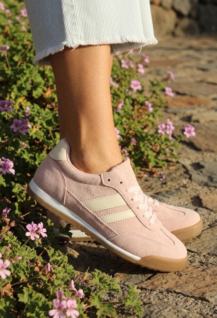 Pink sneakers worn on a stone path with flowers in the background