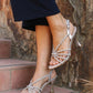 Silver strappy high-heeled sandals worn by a person on stone steps.