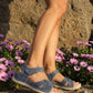 Person wearing blue sandals standing on rocks with pink flowers and a rocky background